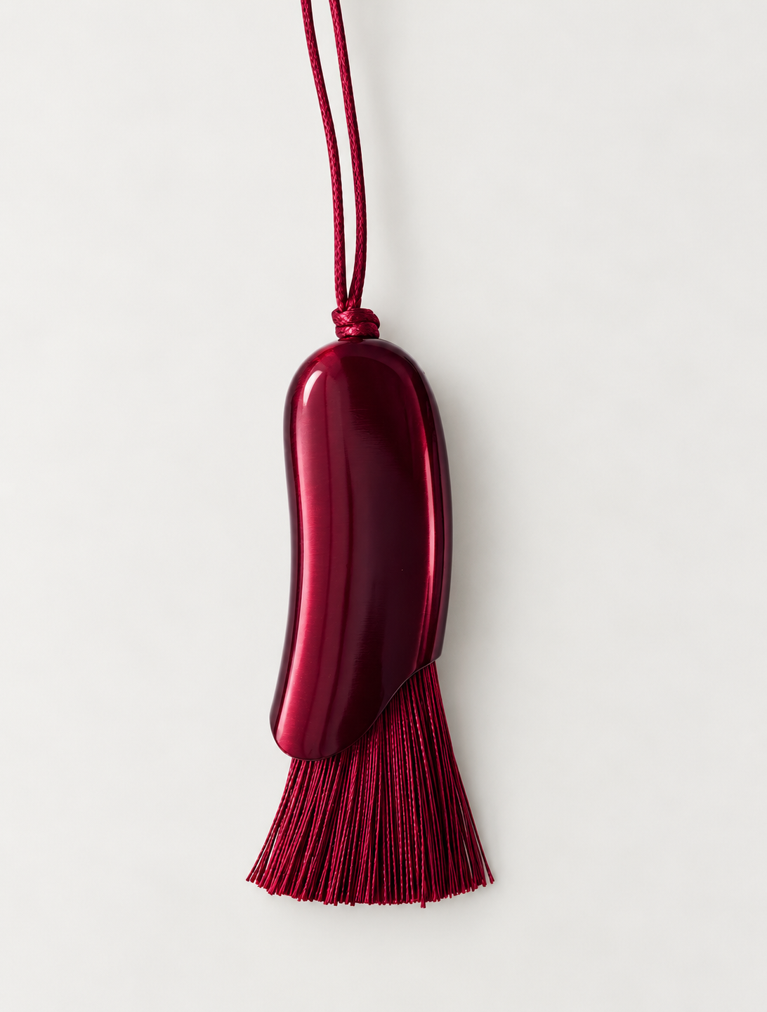 A glossy dark red, bean-shaped pendant with a matching red tassel and cord, shown against a plain light gray background.