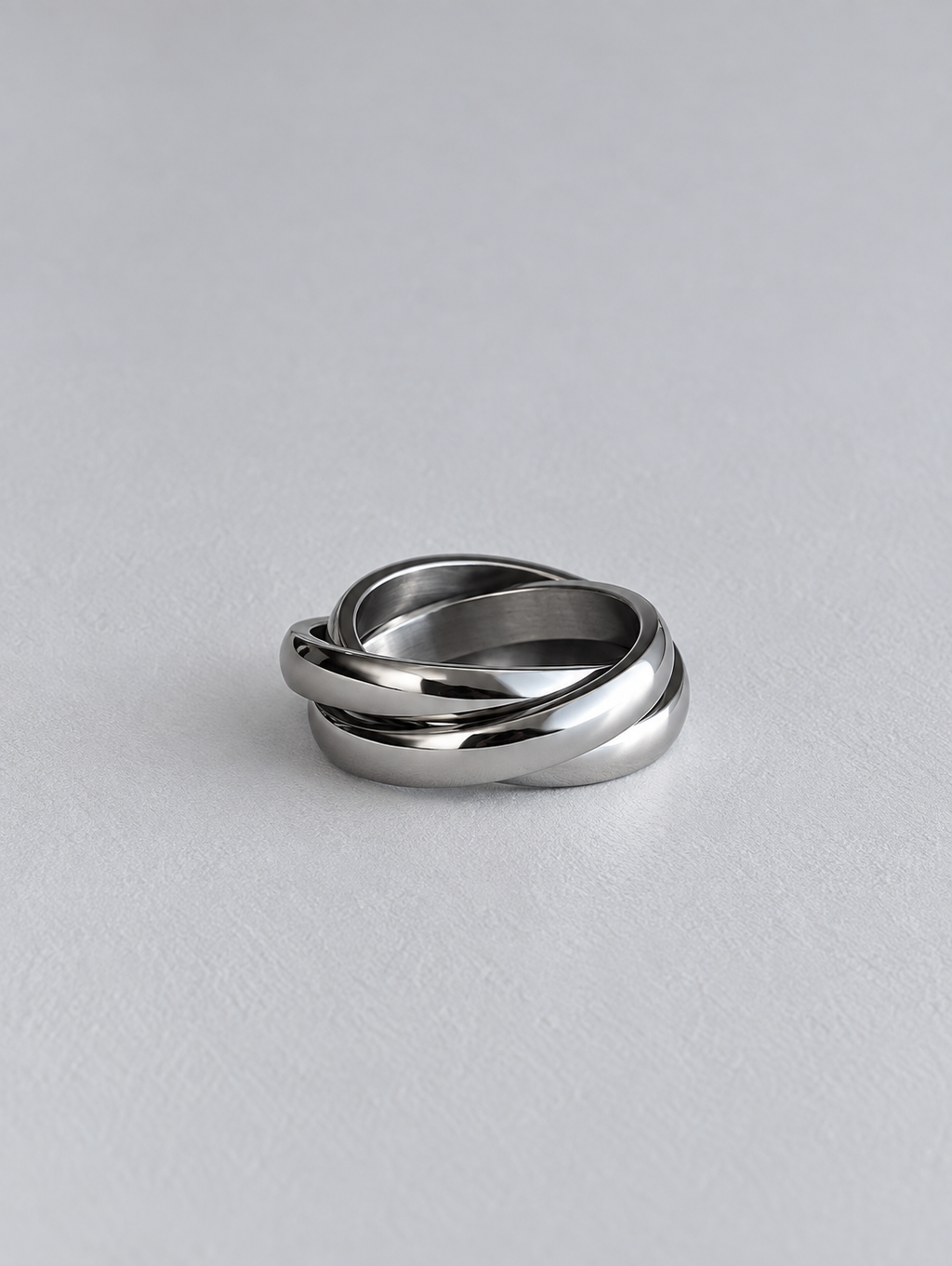 A polished silver-toned metal ring with a twisted knot design, resting on a light gray textured surface.
