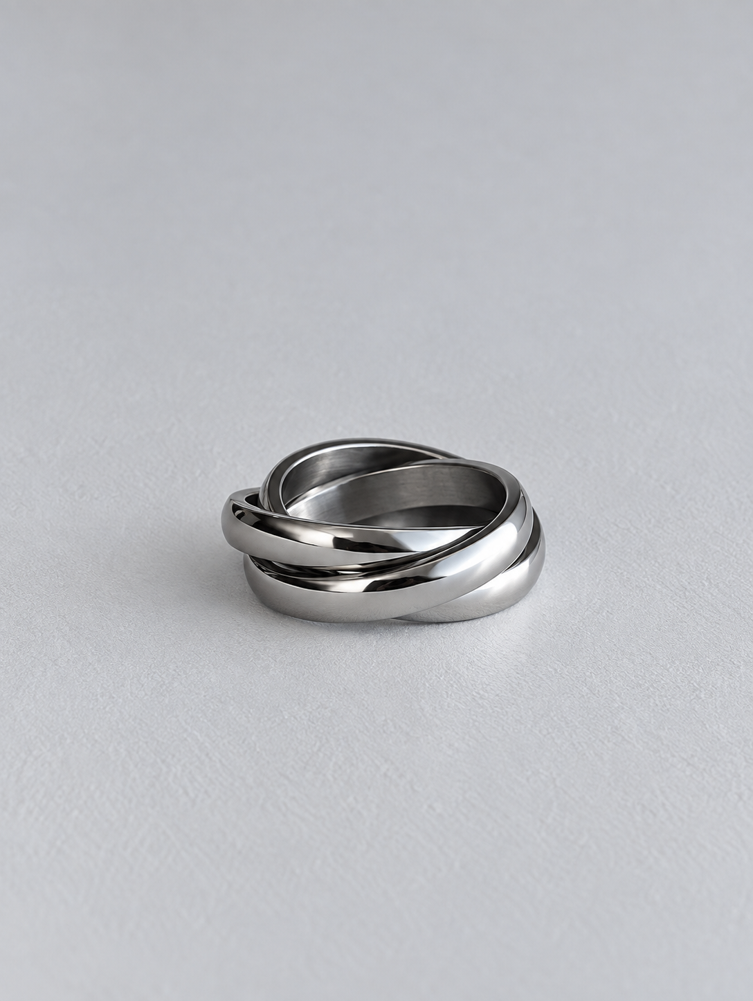 A polished silver-toned metal ring with a twisted knot design, resting on a light gray textured surface.