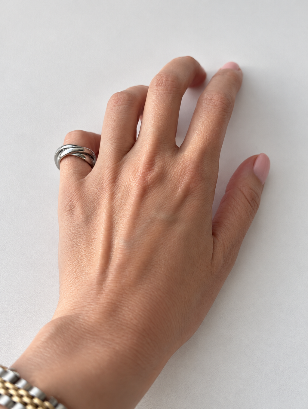 A close-up of a person's hand resting on a light gray surface, wearing a silver-toned wrap-style ring on the ring finger.