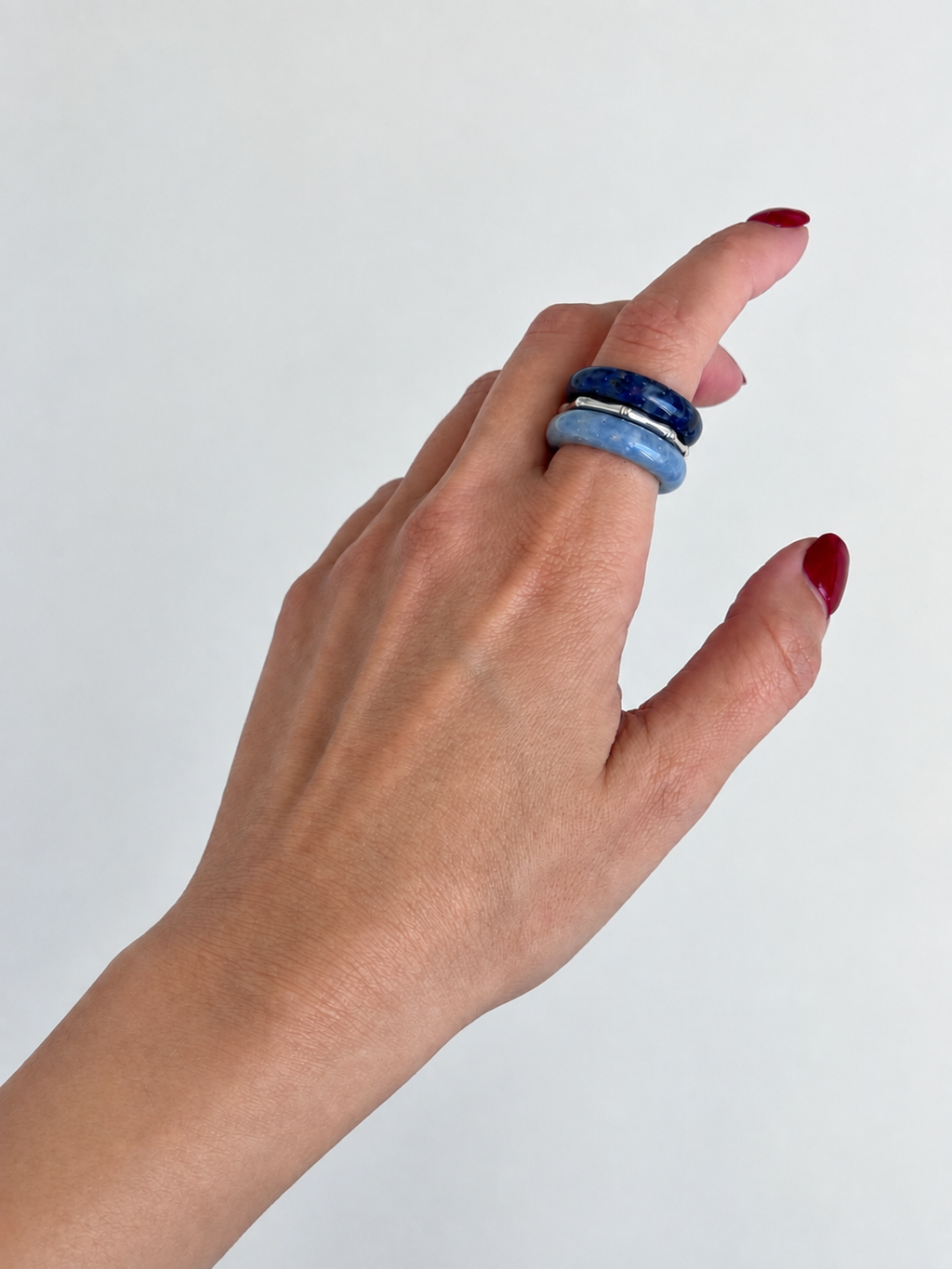 A close-up of a hand wearing two stacked rings, one dark blue and one light blue, against a plain light gray background.