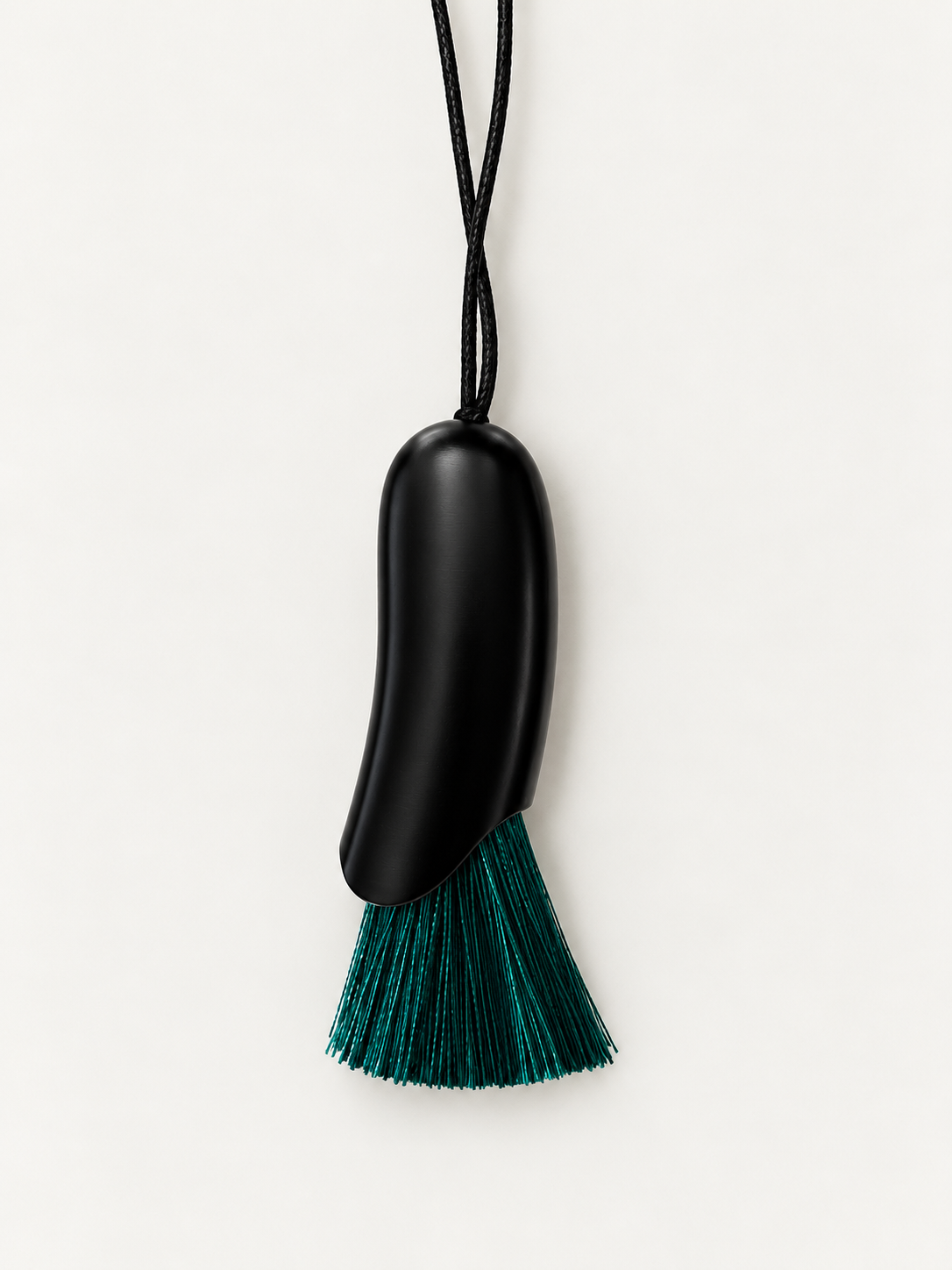 A minimalist black pendant necklace with a smooth, organic-shaped black body and a dangling tassel made of green threads, suspended from a thin black cord against a clean off-white background.