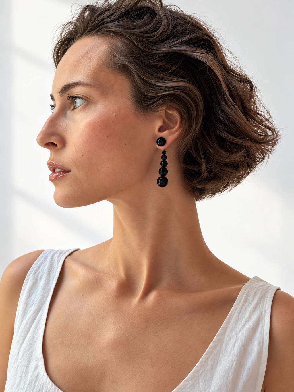 A woman in profile wearing a long black beaded drop earring, photographed in bright natural light against a white background.