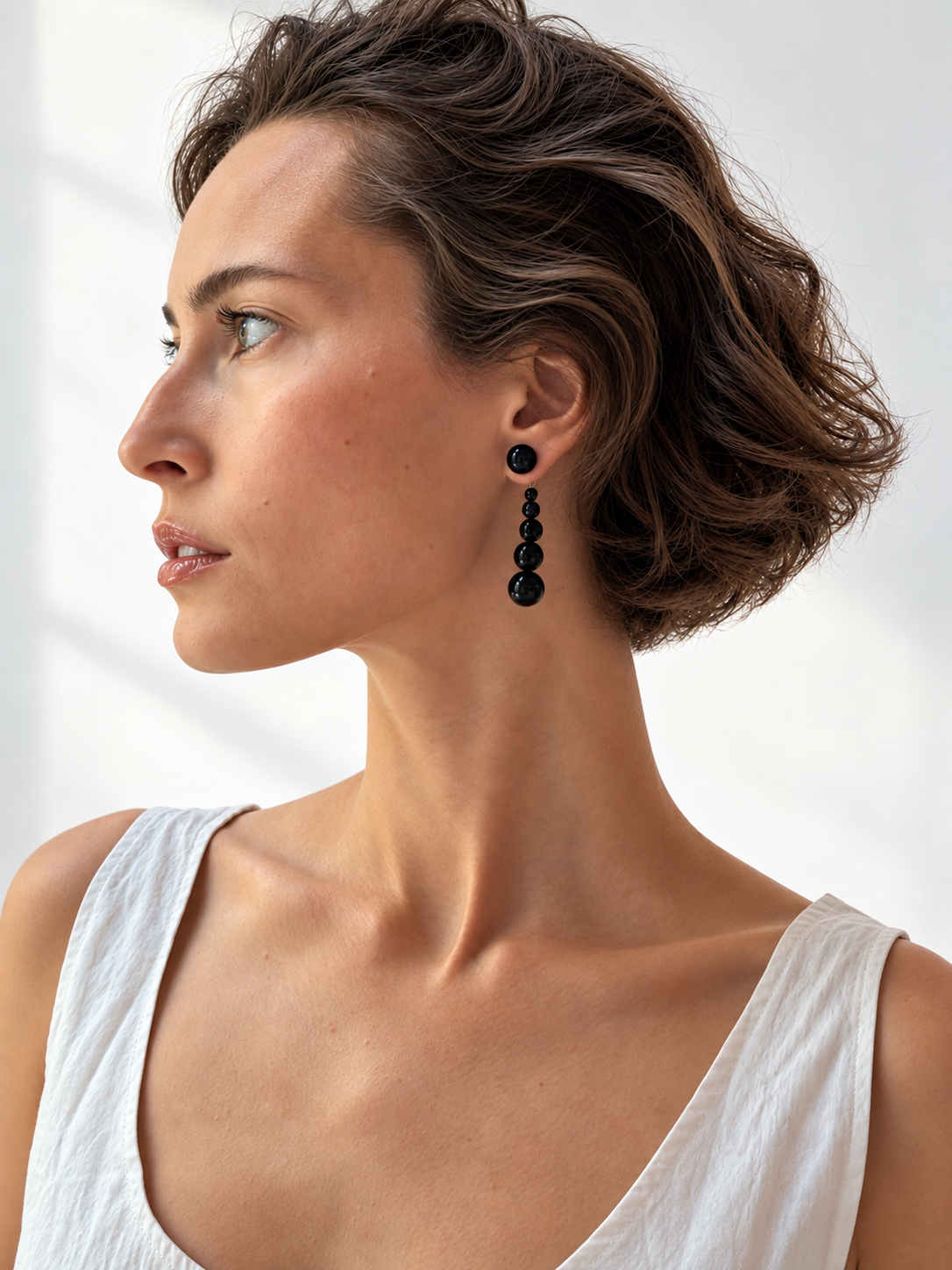 A woman in profile wearing a long black beaded drop earring, photographed in bright natural light against a white background.